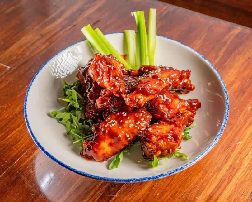 Sweet and spicy chicken wings with sesame seeds, served on a bed of arugula with celery sticks.
