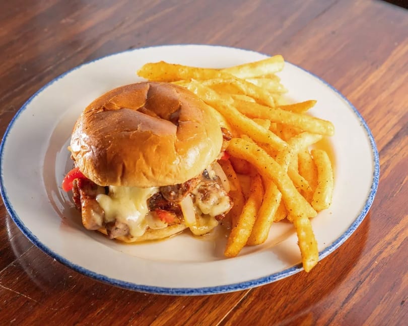 Cheesesteak sandwich with melted cheese, onions, and peppers, served with golden french fries.