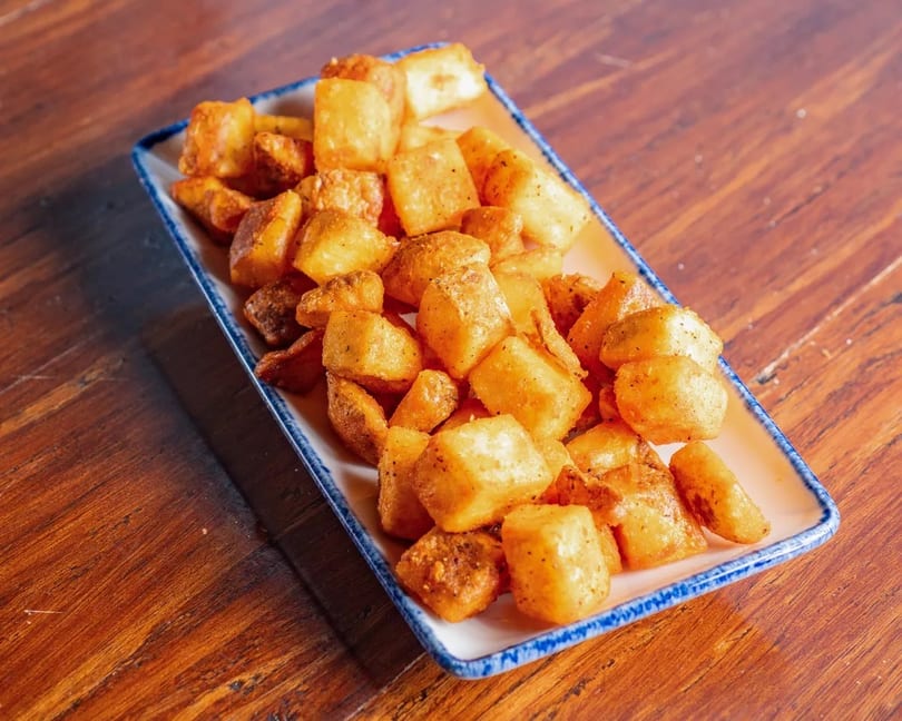 Crispy golden-brown fried potatoes, seasoned with spices, served on a rectangular white plate with blue trim.