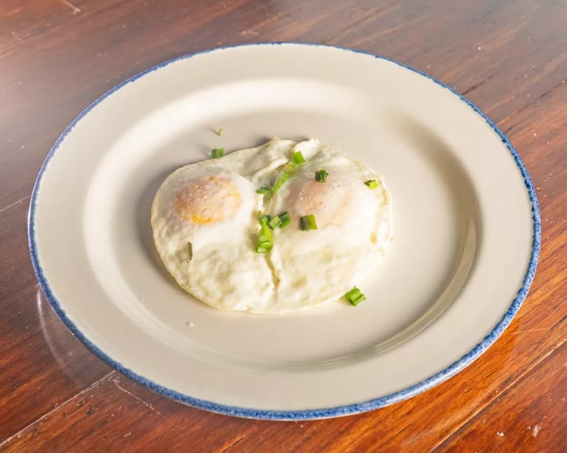 Two sunny-side-up eggs with chopped green onions on a white plate with a blue rim.