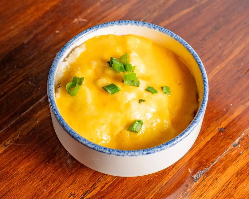 A white bowl with blue trim filled with cheesy grits topped with chopped green onions.