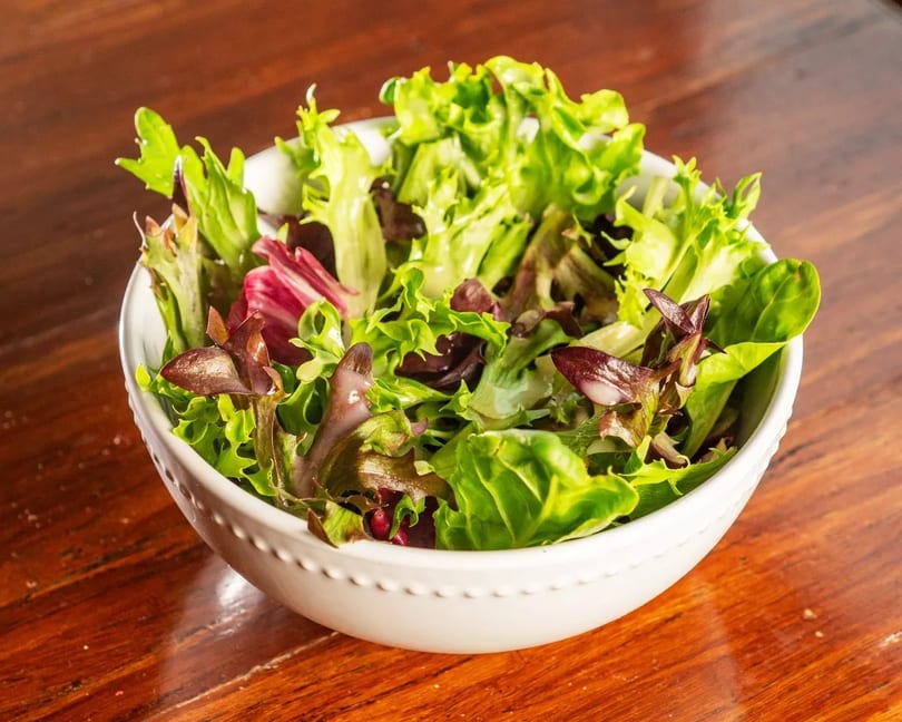 A white bowl filled with fresh green and red leaf lettuce on a wooden table.