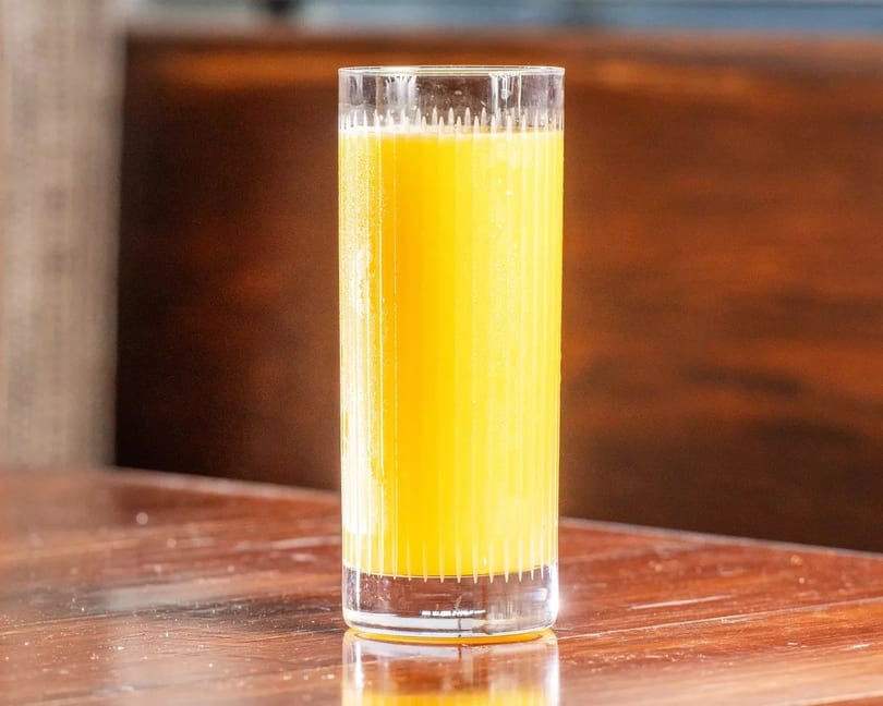 Tall glass of fresh orange juice on a glossy wooden table with a dark background.